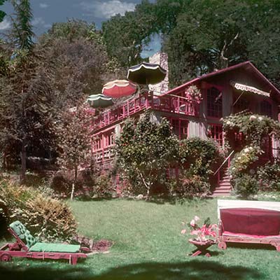 Historic archival photo of Shadowbrook in Capitola, featuring the rustic wooden facade and glowing windows as seen from the garden trails, capturing the 'treehouse' aesthetic of the original building.