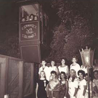 A vintage black-and-white photograph of a group of beauty contestants in sashes and evening gowns posing on the garden stairs at Shadowbrook Restaurant, showcasing a mid-century community event.