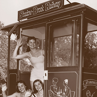 A vintage black-and-white photograph of beauty contestants in sashes posing and smiling from inside the iconic Shadowbrook hillside cable car during a historic promotional event.