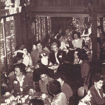 A vintage black-and-white photograph of a crowded dining room at Shadowbrook Restaurant, showing guests in mid-century formal attire enjoying dinner and drinks in a lively, packed atmosphere.
