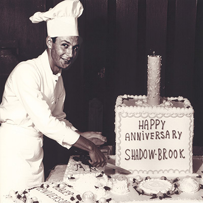 A vintage black-and-white photograph of the Shadowbrook owner cutting a large ceremonial anniversary cake to celebrate a milestone year for the restaurant.