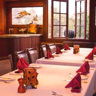 Elegantly set private dining room with wood paneling, white tablecloths, red napkins, and a stained glass window depicting ducks.