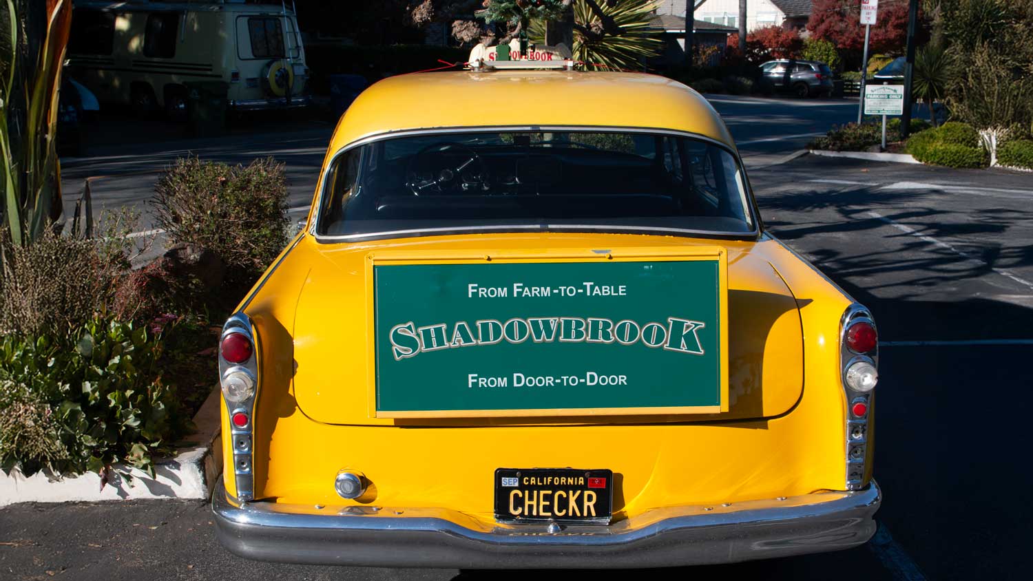 The back of a vintage Shadowbrook Restaurant wood-paneled taxi, featuring the gold and green logo and custom 'CHECKR' license plate.