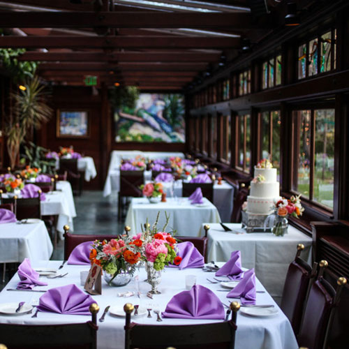 alt="A wedding reception at Shadowbrook Restaurant with tables set for a formal dinner, featuring candlelit ambiance and large windows overlooking the lush forest gardens.